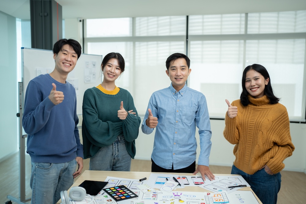 Asian team ux developer and ui designer brainstorming about mobile app interface wireframe design on table with customer brief and color code at modern office.