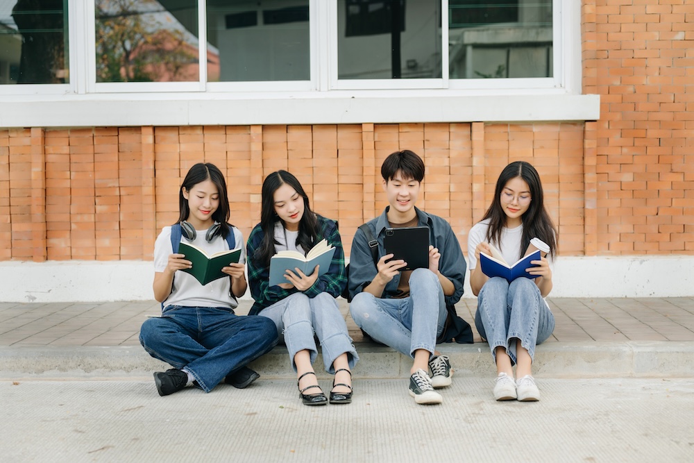 Young Asian college students and a female student group work at the campus park